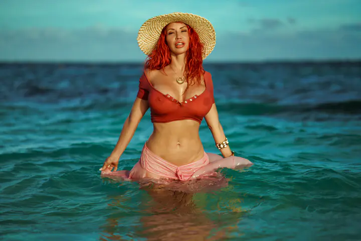 Bianca Beauchamp in a straw hat, standing in a turquoise sea